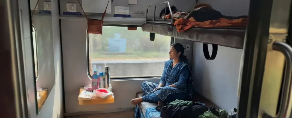 Woman sitting cross-legged on a lower berth inside an Indian Railways 1AC train compartment.